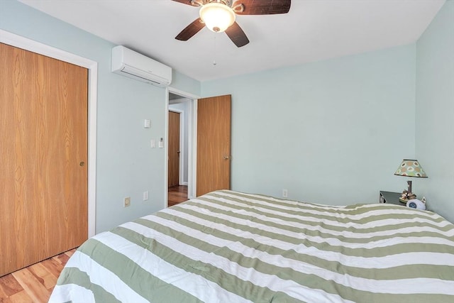 bedroom with an AC wall unit, wood finished floors, a ceiling fan, and a closet