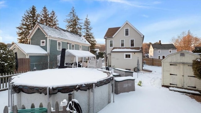 snow covered rear of property featuring a storage shed and a covered pool