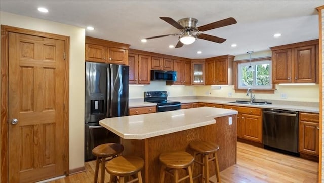 kitchen with a breakfast bar, sink, a center island, light hardwood / wood-style floors, and black appliances