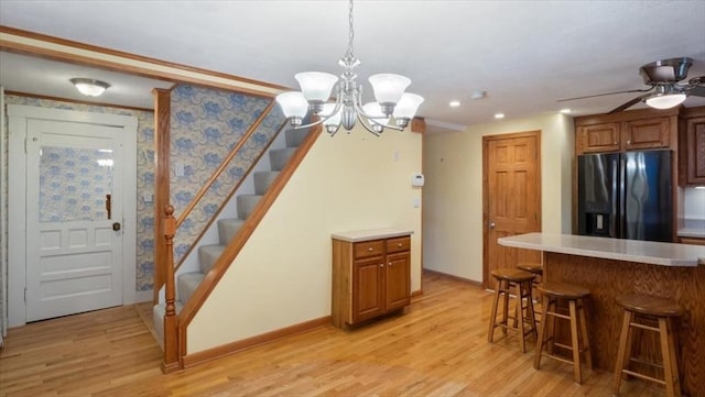 kitchen featuring ceiling fan with notable chandelier, pendant lighting, a kitchen bar, black refrigerator with ice dispenser, and light hardwood / wood-style flooring