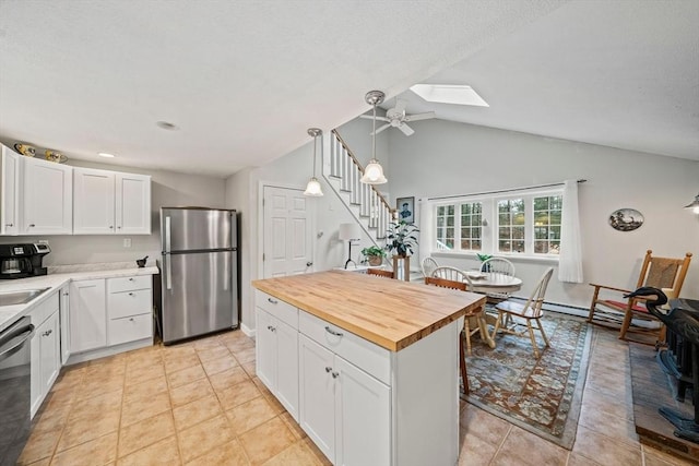 kitchen with pendant lighting, lofted ceiling with skylight, white cabinets, butcher block countertops, and stainless steel appliances