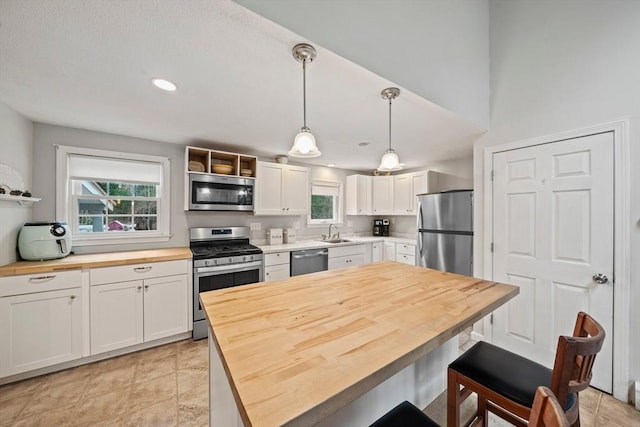 kitchen with butcher block countertops, white cabinets, stainless steel appliances, and decorative light fixtures