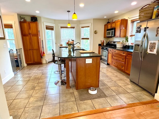 kitchen with a breakfast bar, a baseboard heating unit, an island with sink, appliances with stainless steel finishes, and decorative light fixtures