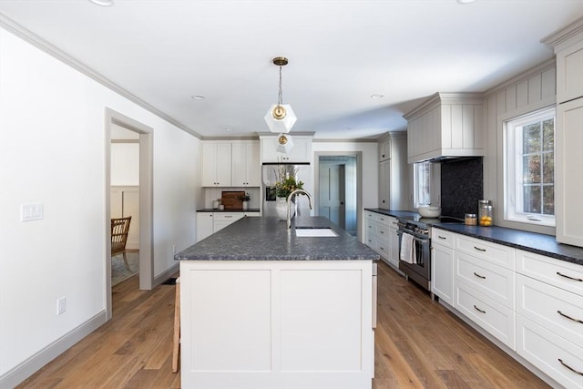 kitchen featuring sink, hanging light fixtures, a kitchen island with sink, stainless steel appliances, and light wood-type flooring