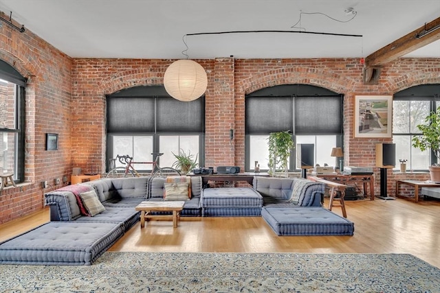 living area featuring wood finished floors, brick wall, and beamed ceiling