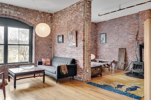 living room featuring a wood stove, brick wall, and wood finished floors