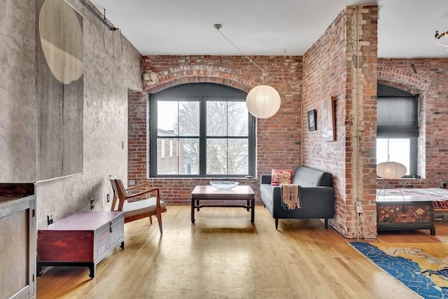 sitting room with wood finished floors, healthy amount of natural light, and brick wall