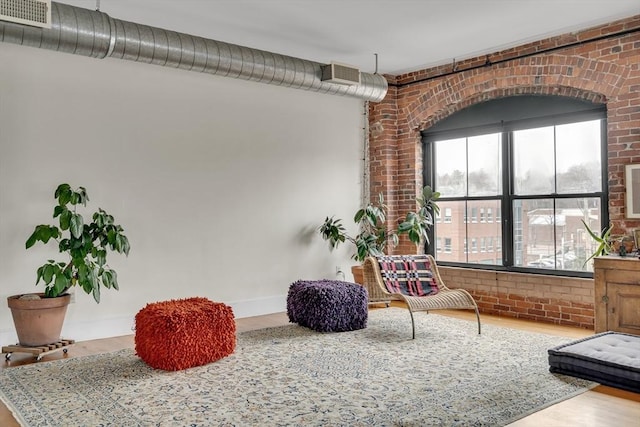 sitting room with wood finished floors, brick wall, and baseboards