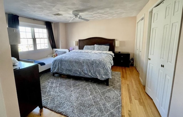 bedroom featuring visible vents, two closets, a textured ceiling, and wood finished floors