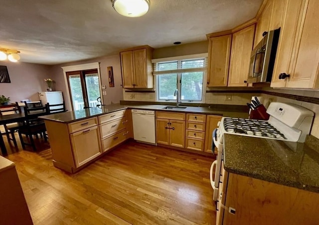 kitchen with a sink, white appliances, a peninsula, and wood finished floors