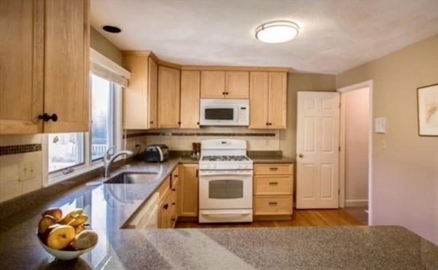 kitchen with white appliances, light brown cabinets, a sink, decorative backsplash, and dark countertops