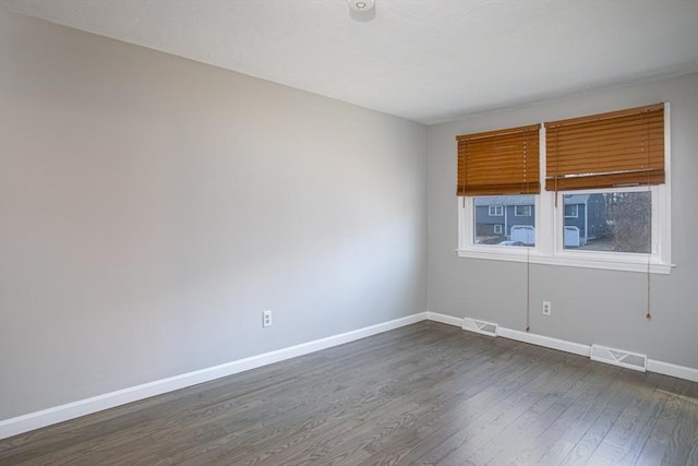 spare room featuring dark wood finished floors, visible vents, and baseboards