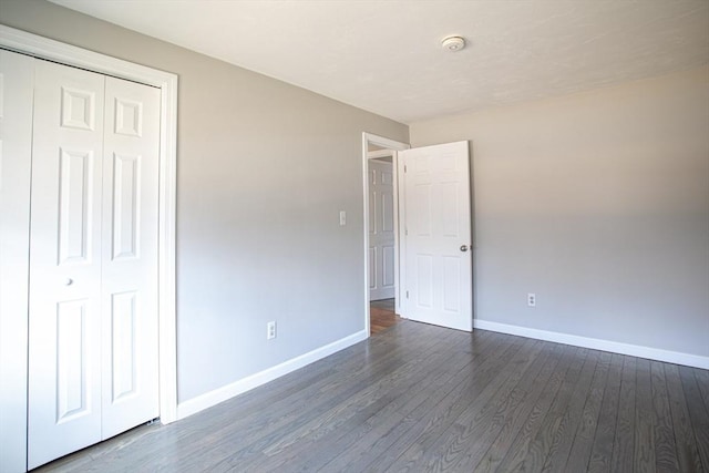 unfurnished bedroom featuring dark wood-style flooring, a closet, and baseboards