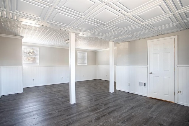 basement featuring an ornate ceiling, wainscoting, visible vents, and dark wood-type flooring