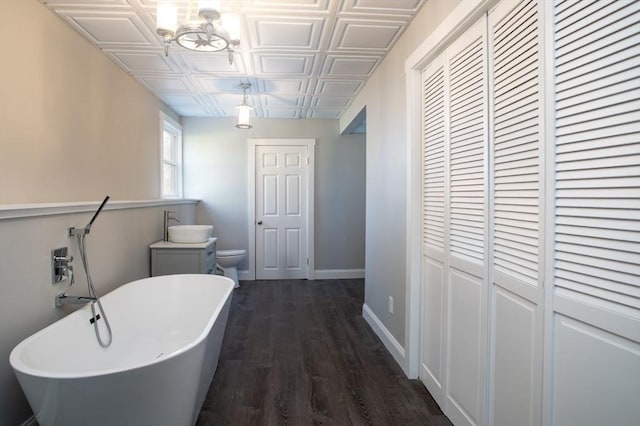 bathroom featuring an ornate ceiling, a soaking tub, toilet, wood finished floors, and baseboards