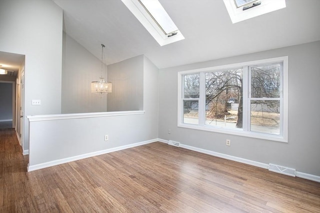 empty room featuring baseboards, vaulted ceiling with skylight, visible vents, and wood finished floors