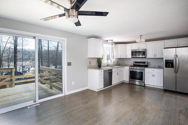 kitchen with dark wood finished floors, stainless steel appliances, white cabinets, a sink, and baseboards