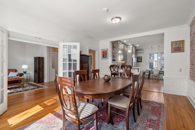 dining space featuring a wainscoted wall, ornamental molding, hardwood / wood-style flooring, french doors, and a decorative wall