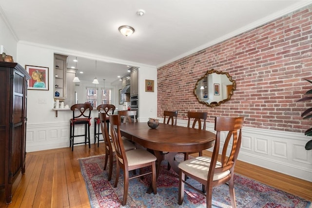 dining room featuring brick wall, a wainscoted wall, wood-type flooring, and ornamental molding