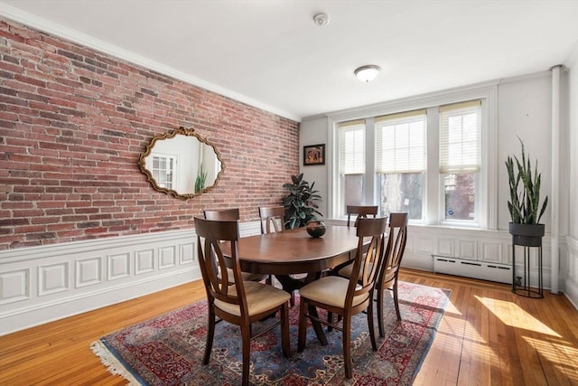 dining space with brick wall, hardwood / wood-style flooring, wainscoting, crown molding, and baseboard heating