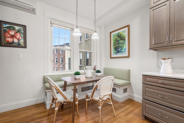 dining area with a wall unit AC, light wood-style flooring, baseboards, and breakfast area