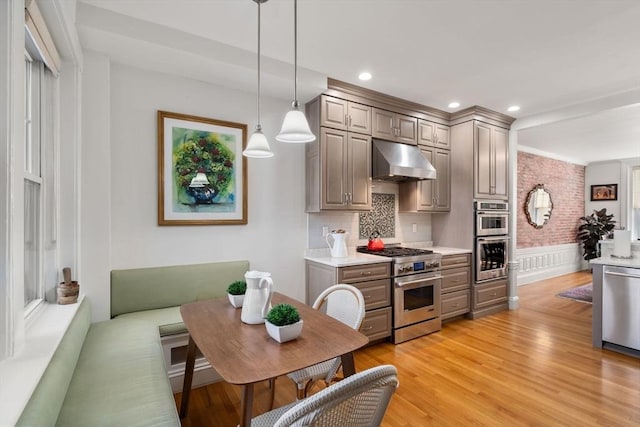 kitchen featuring light wood-type flooring, under cabinet range hood, stainless steel appliances, light countertops, and hanging light fixtures