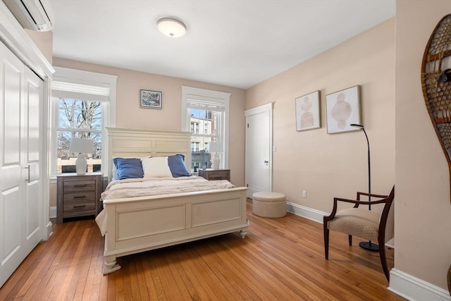 bedroom featuring light wood-style floors, baseboards, and a wall mounted air conditioner