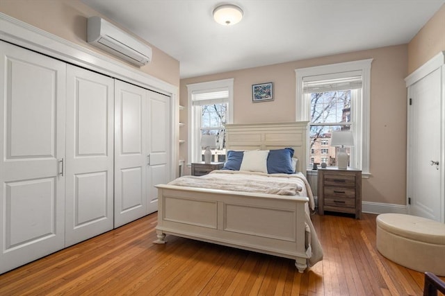 bedroom with a closet, baseboards, a wall mounted AC, and light wood-style floors