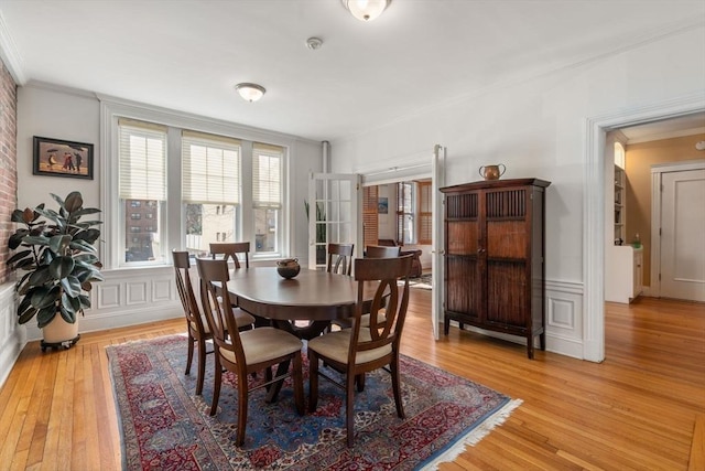 dining space with a decorative wall, light wood-type flooring, and ornamental molding