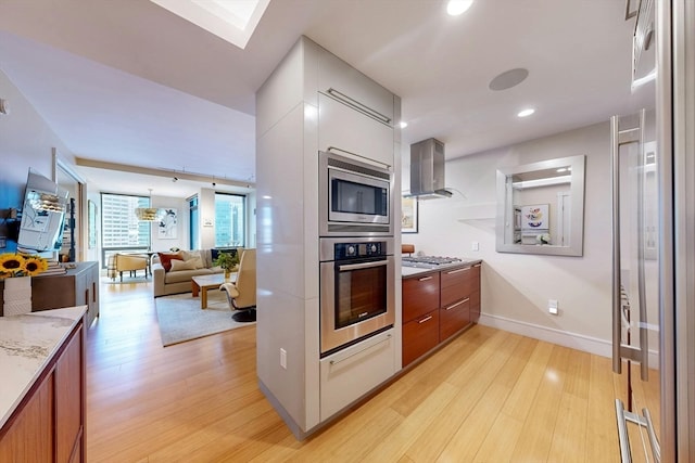 kitchen with appliances with stainless steel finishes, light hardwood / wood-style floors, wall chimney range hood, and a skylight