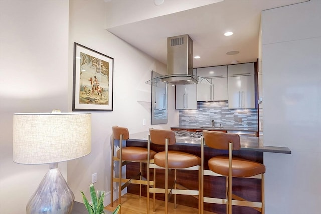 kitchen with backsplash, light hardwood / wood-style floors, island exhaust hood, kitchen peninsula, and gray cabinets