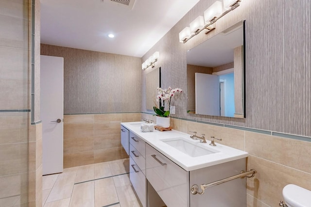 bathroom with tile walls, tile patterned flooring, dual bowl vanity, and toilet