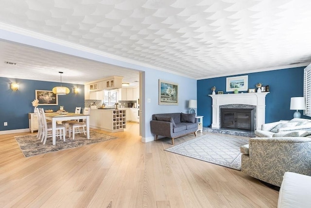 living area with light wood-style flooring, a fireplace, visible vents, and crown molding