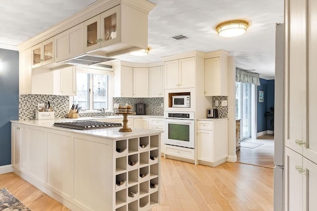 kitchen featuring a peninsula, white appliances, visible vents, and light wood finished floors