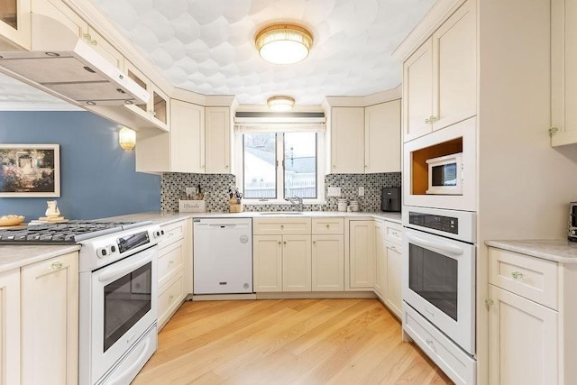 kitchen featuring light wood-style flooring, white appliances, a sink, light countertops, and tasteful backsplash