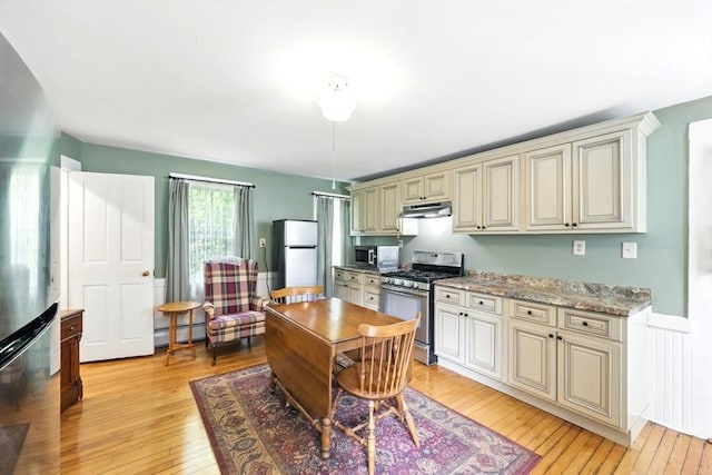 96 College St, South Hadley, MA 01075 - kitchen featuring appliances with stainless steel finishes, cream cabinetry, under cabinet range hood, a baseboard radiator, and wainscoting