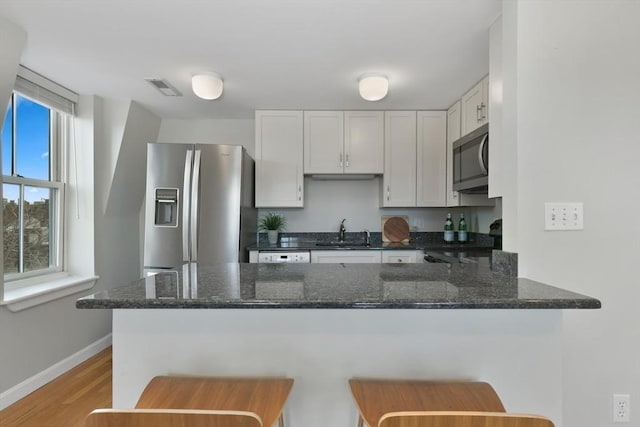 kitchen with sink, appliances with stainless steel finishes, a kitchen breakfast bar, kitchen peninsula, and white cabinets