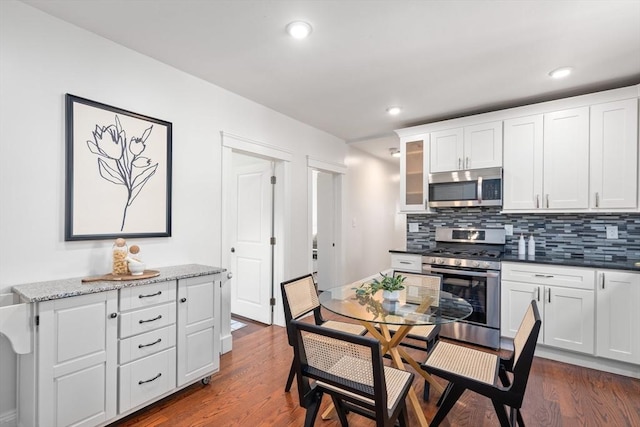 kitchen featuring glass insert cabinets, dark wood finished floors, decorative backsplash, stainless steel appliances, and white cabinetry