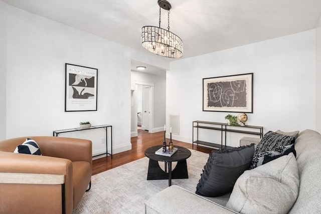 living room featuring a chandelier, visible vents, baseboards, and wood finished floors