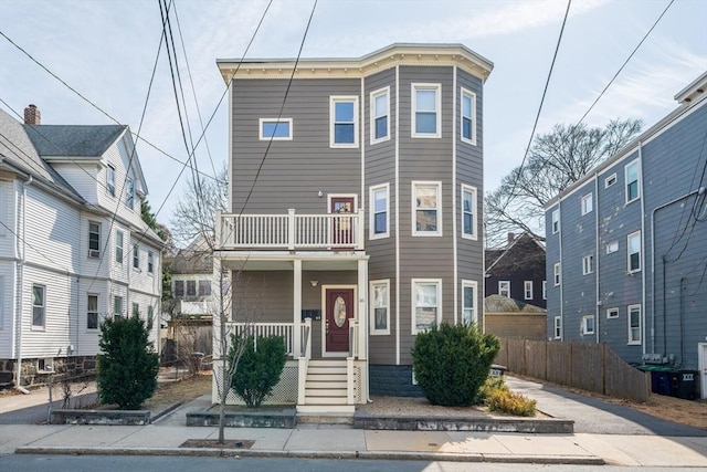 view of property featuring a porch, a balcony, and fence