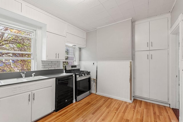 kitchen with beverage cooler, stainless steel gas range, a sink, light wood-style floors, and white cabinets