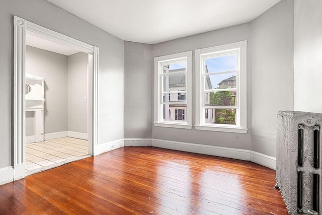 unfurnished living room with radiator heating unit, hardwood / wood-style floors, and baseboards