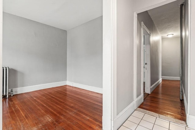 hallway featuring hardwood / wood-style flooring, baseboards, and radiator heating unit