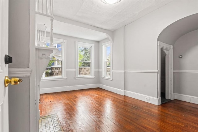 interior space featuring wood-type flooring, baseboards, and arched walkways