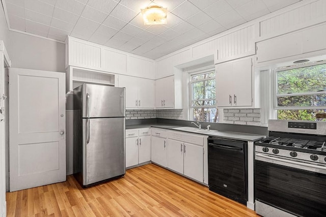 kitchen featuring stainless steel appliances, a sink, dark countertops, light wood-style floors, and white cabinets