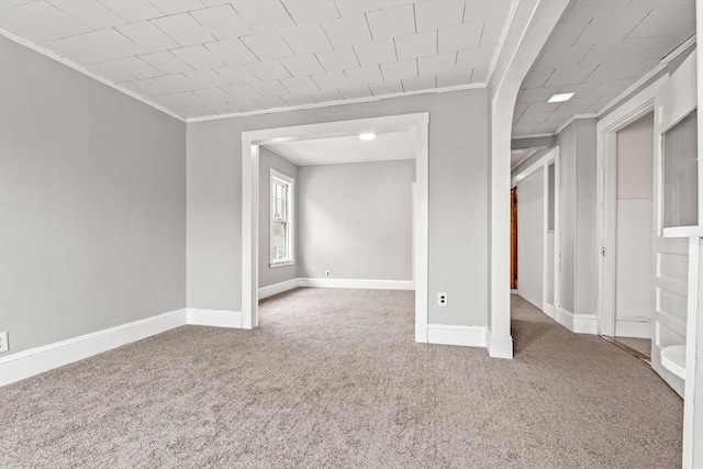 carpeted spare room featuring crown molding and baseboards
