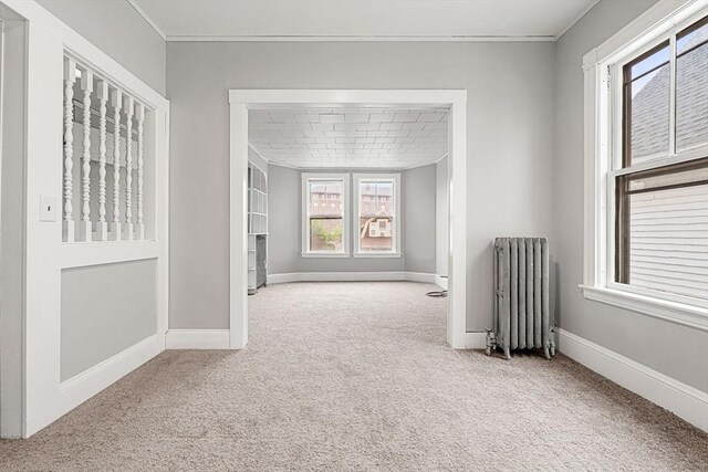 carpeted empty room with radiator heating unit, crown molding, and baseboards