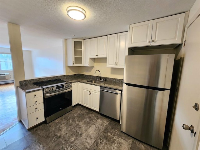 kitchen featuring appliances with stainless steel finishes, a textured ceiling, sink, dark stone countertops, and white cabinetry