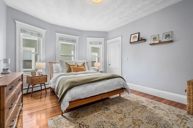 bedroom featuring baseboard heating, baseboards, and wood finished floors