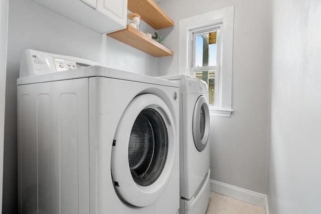 washroom featuring washer and clothes dryer, baseboards, light tile patterned flooring, and cabinet space